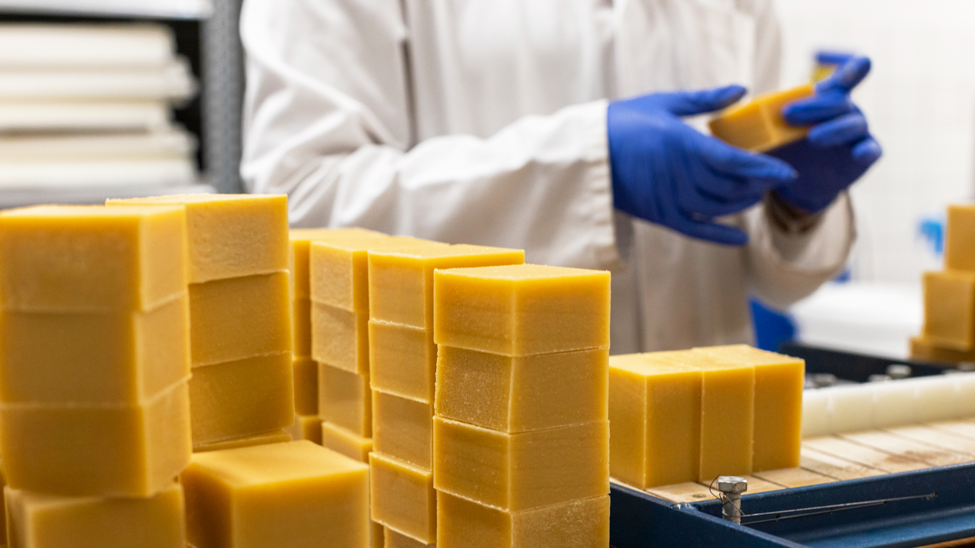 Pavés de savon empilés en cure, une personne en blouse et gants bleus en arrière-plan